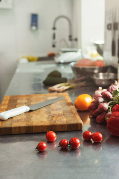 Cooking healthy meals at professional kitchen. Organic vegetables, wooden cutting board, sharp chef knife on steel table