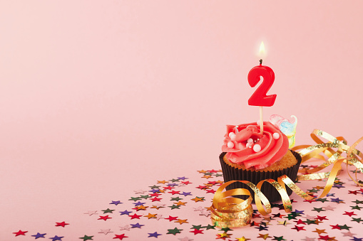 Second birthday cupcake with candle and sprinkles on pink background. Card mockup, copy space. Birthday, party, holiday concept