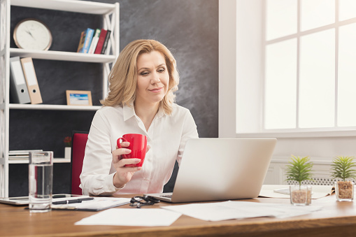 Businesswoman working on laptop at office and having coffee while sitting at her working place, copy space
