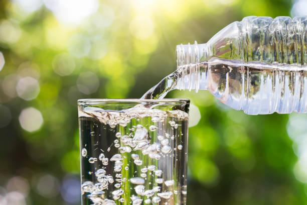istock Drinking water pouring from bottle into glass on blurred fresh green nature bokeh background, healthy drink concept 931723864