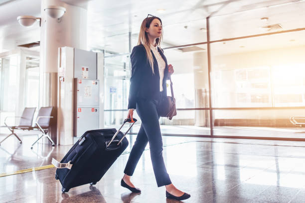istock Elegant young woman walking and pulling her suitcase in the airport terminal 931743922