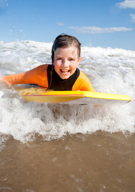 Little girl Bodyboarding in the Sea Little girl is smiling for the camera as she bodyboards in the sea. body board stock pictures, royalty-free photos & images