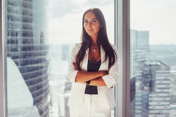 retrato de mulher de negócios elegante vestindo terno formal branco em pé perto da janela, olhando para a câmera - executive apartment - fotografias e filmes do acervo