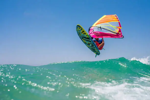 Young man jumping on waves with windsurfing board and colourful sail.