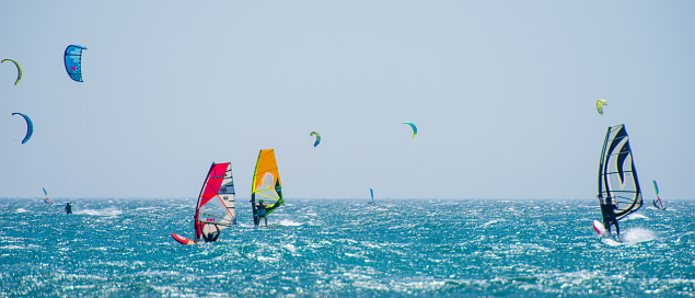 Group of people doing kitesurfing and windsurfing on sea.