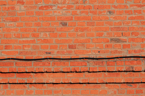 Red brick wall with corrugated pipe for electrical wiring as background or texture