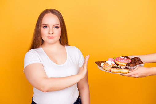 ¡Estoy en contra de comer productos que contengan grasa! Voluntad-powered mujer vestida con camiseta blanca se niega a consumir sabrosos deliciosos dulces en un plato, aislado sobre fondo amarillo brillante photo