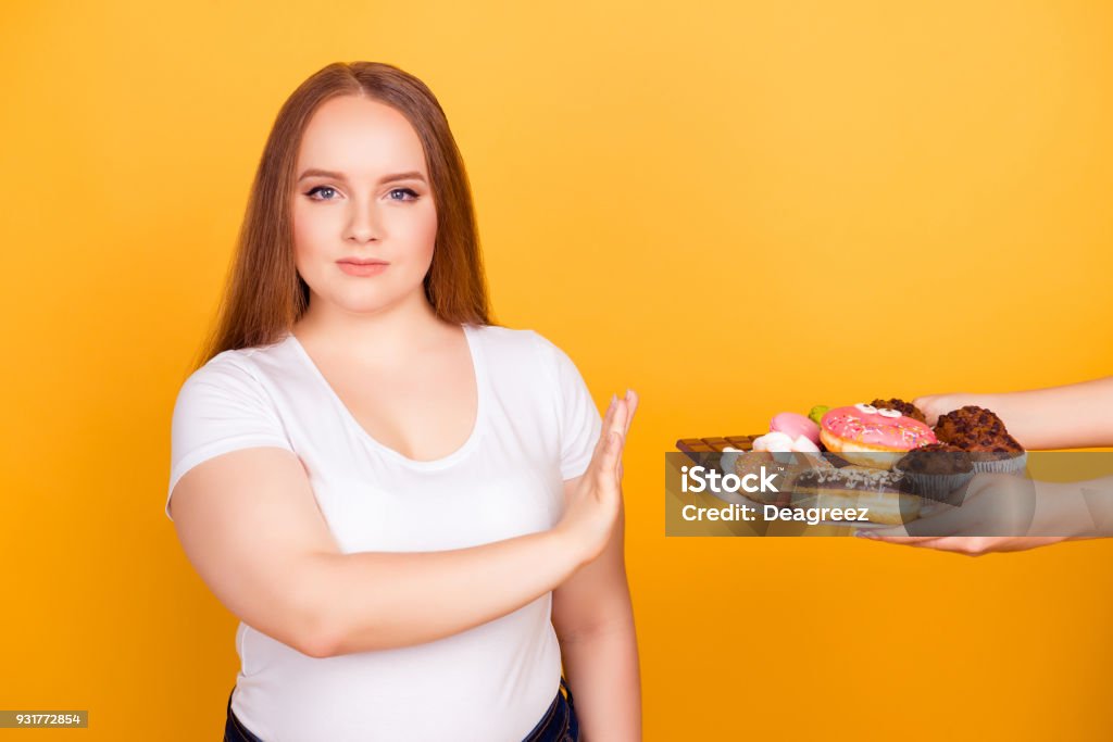 Je suis contre la consommation de produits contenant de la graisse ! Femme de volonté-powered portant tshirt blanc refuse de consommer de délicieux délicieux gâteaux sur une plaque, isolé sur un fond jaune clair - Photo de Surpoids libre de droits