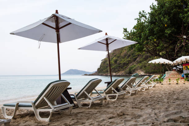 istock Beach chairs and white umbrella in sand with bright sunlight 931779296