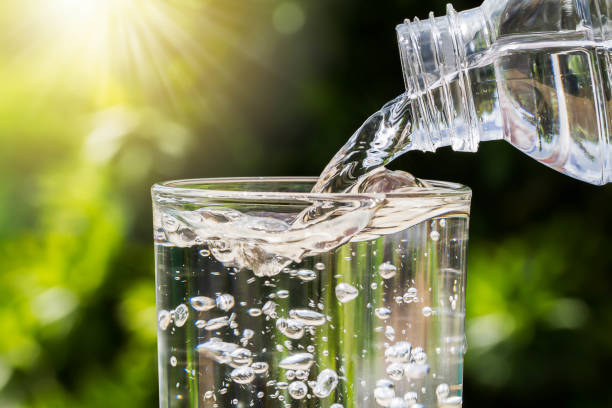 istock Drinking water pouring from bottle into glass on blurred green nature background 931779314