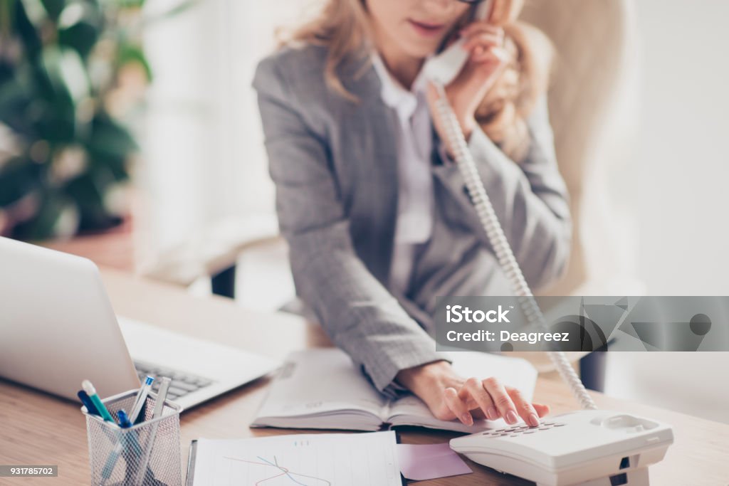 Cropped closeup photo of clever smart professional polite secretary in grey formal suit is calling to her boss, she is sitting at the table in office Secretary Stock Photo