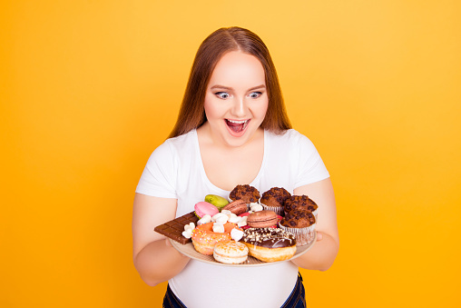 Yummy! I'm a sweet-tooth! Portrait of excited cheerful with open mouth fatty lady looking at plate full of tasty delicious aromatic biscuits candies and cookies, isolated on bright yellow background