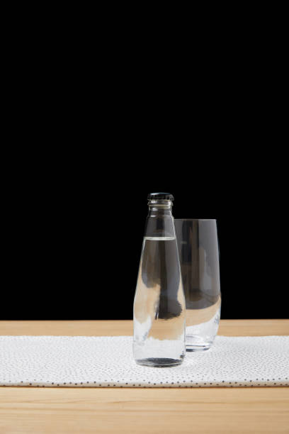 istock Bottle with water and empty glass on table on black background 931790416