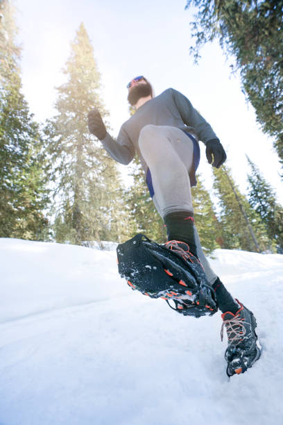 Low angle view of bearded man trail running in winter with rubber cleats on his tennis shoes to aid traction in the snow, Hyalite Canyon Recreational Area, Bozeman, Montana, USA