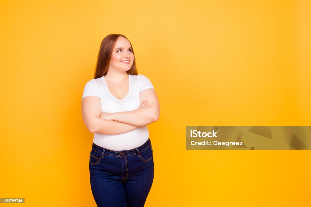 Happy cheerful joyful confident with chubby face oversize woman wearing casual tshirt and dark blue jeans, standing with folded arms, looking at empty blank space isolated on bright yellow background Women Stock Photo