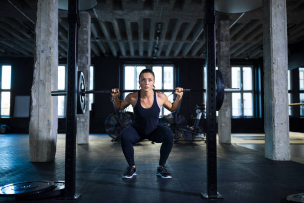 #VALUE! Determined woman crouching while exercising with barbell. Female athlete is working hard in gym. She is doing weightlifting. woman weight training stock pictures, royalty-free photos & images