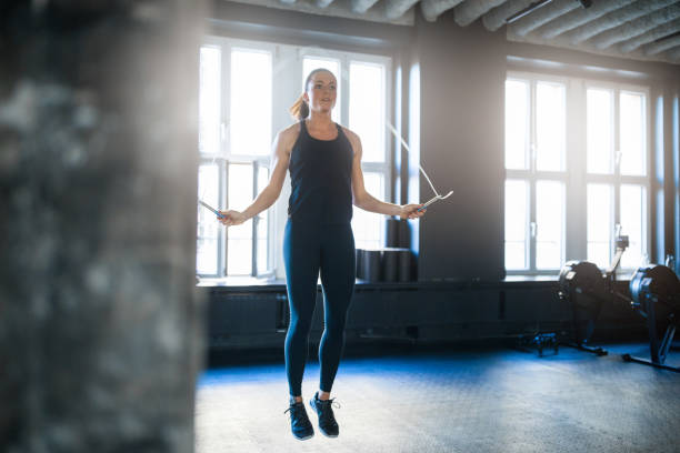 Sporty woman doing workout with jump rope in gym Young woman doing workout with jump rope in gym. Determined female athlete is exercising at health club. She is in sports clothing. jump rope stock pictures, royalty-free photos & images