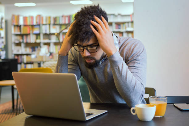 istock Young student getting frustrated over laptop in library 931805242