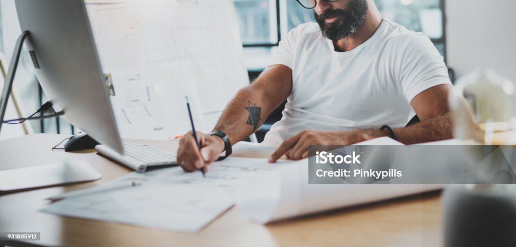 Bearded professional architect wearing eye glasses working at modern loft studio-office with desktop computer.Blurred background. Horizontal.Cropped. Bearded professional architect wearing eye glasses working at modern loft studio-office with desktop computer.Blurred background. Horizontal.Cropped Design Professional Stock Photo