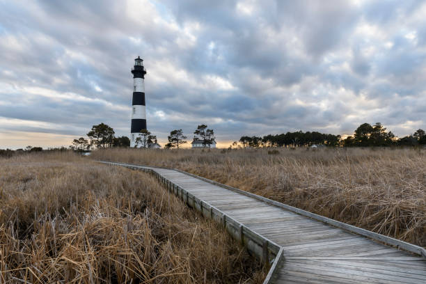 Bodie Lighthouse in Winter with Storm Clouds Wooden walkway to lighthouse with dramatic clouds at sunset - Bodie lighthouse in Cape Hatteras National Seashore, North Carolina. bodie island stock pictures, royalty-free photos & images