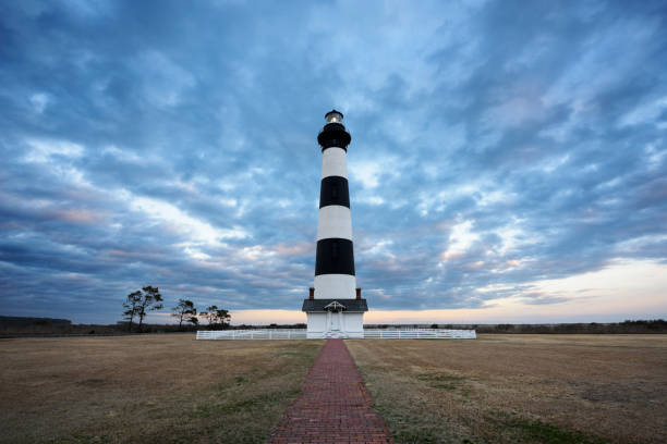 Dramatic Sunset Sky at Lighthouse - Cape Hatteras National Seashore Bodie Lighthouse on the Outer Banks of North Carolina with brick walkway leading to it at sunset. bodie island stock pictures, royalty-free photos & images