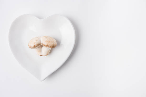 raw mushrooms laying on heart shaped plate on white background