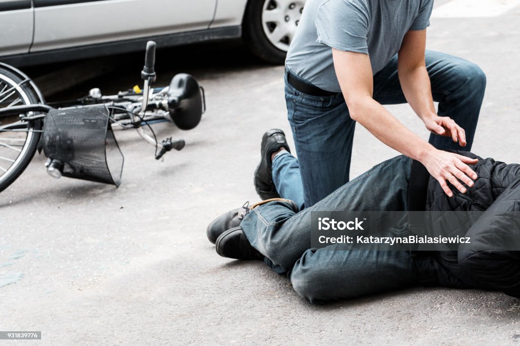 Pedestrian helping accident victim Pedestrian helping a victim of an automobile accident lying on the street next to a broken bike Crash Stock Photo