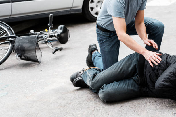 Pedestrian helping accident victim Pedestrian helping a victim of an automobile accident lying on the street next to a broken bike pedestrian stock pictures, royalty-free photos & images