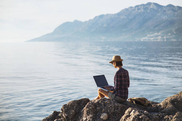istock Young woman using laptop near the sea 931845070