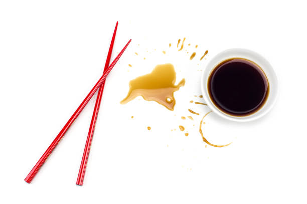 Red Japanese chopsticks sushi and soy sauce spilled splash from bowl isolated on white background