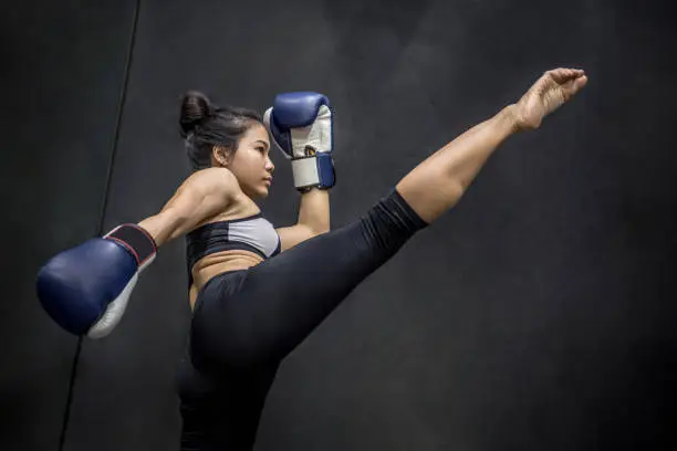Photo of Young Asian woman boxer with blue boxing gloves kicking in the exercise gym