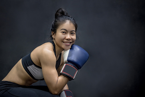 Beautiful young Asian woman posing with blue boxing gloves, black background
