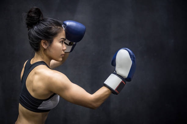 young Asian woman posing with blue boxing gloves Beautiful young Asian woman posing with blue boxing gloves, black background boxercise stock pictures, royalty-free photos & images