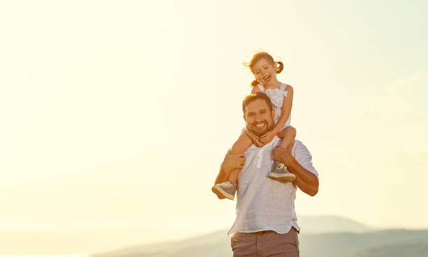 istock father's day. child daughter sits on her dad shoulders outdoors on a summer 931868720