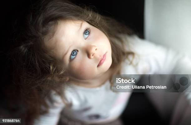 A Little Toddler Girl Looking Up Serious By The Window Stock Photo - Download Image Now