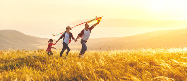 feliz familia padre, madre hijo hija y lanzar una cometa en naturaleza al atardecer - family nature healthy lifestyle happiness fotografías e imágenes de stock