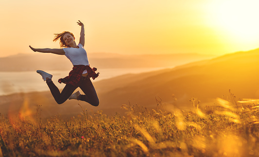 Happy woman jumping and enjoying life in field at sunset in mountains