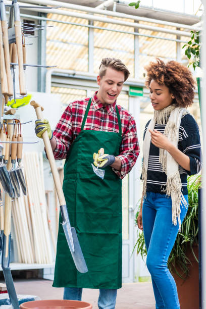 handsome worker helping a customer with choosing a gardening tool - florist flower market flower store imagens e fotografias de stock