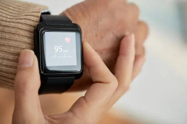 Close-up shot of unrecognizable doctor checking pulse of her senior patient with help of smart watch, blurred background