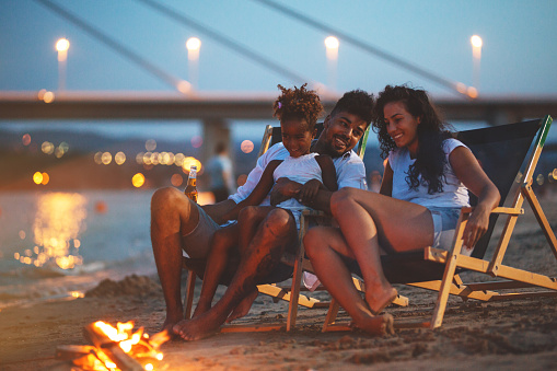 Young mixed race family sitting and relaxing at the beach on beautiful evening.They sitting by the camp fire.