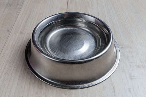 Steel dog bowl with water on wooden floor. Perspective view.