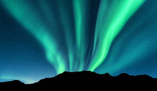 Aurora borealis and silhouette of mountains Aurora and silhouette of mountains. Lofoten islands, Norway. Aurora borealis. Green northern lights. Sky with stars and polar lights. Night landscape with beautiful aurora, blue sky. Nature background brightly lit winter season rock stock pictures, royalty-free photos & images