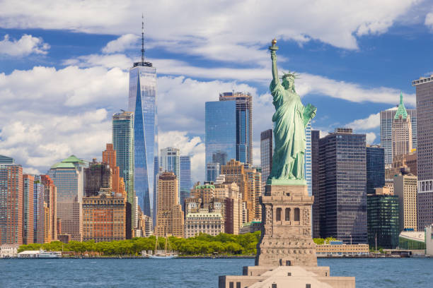 freiheitsstatue und skyline von new york mit manhattan financial district, world trade center, wasser des hafen von new york, battery park und blauer himmel. - world trade center manhattan stock-fotos und bilder