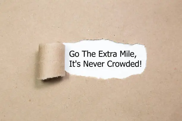 Photo of Motivational quote Go The Extra Mile It's Never Crowded appearing behind ripped paper.