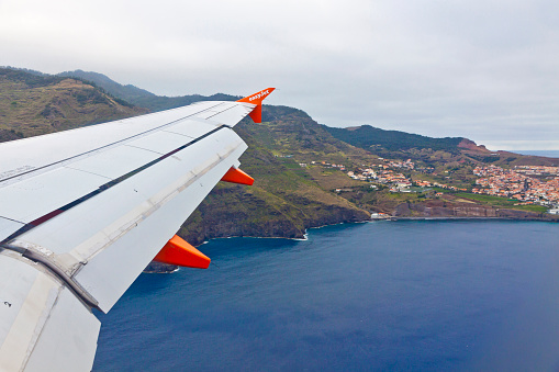 FUNCHAL, PORTUGAL - JUNE 14, 2013: Wing of Airbus A320 plane (operated by EasyJet, flight number EZY 7603) seen during flight over Madeira island. View of Atlantic ocean coast through airplane window