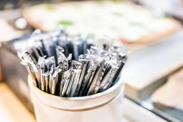 Macro closeup of many black plastic spoons wrapped in plastic packaged fast food in cup container in restaurant
