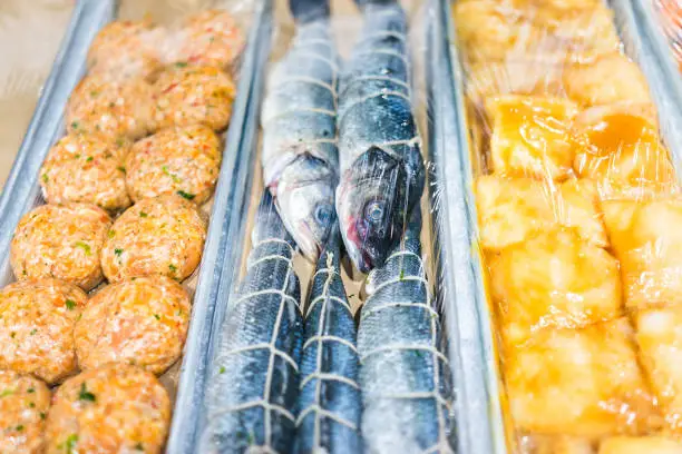 Closeup of many herring fish whole eyes plastic wrapped, cakes burgers in seafood market display