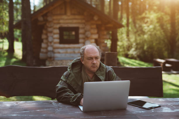 hombre de negocios con ordenador portátil durante sus vacaciones cerca de su casa de verano - guardabosque trabajador de fincas fotografías e imágenes de stock