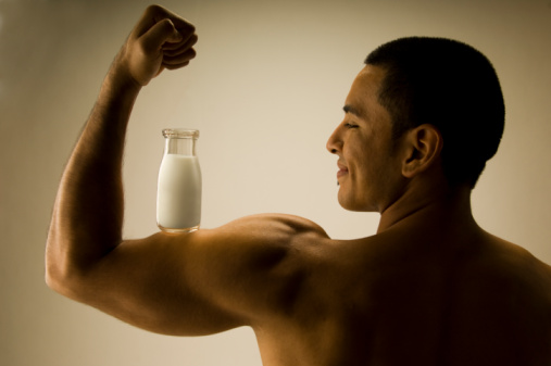 A muscular man balancing a bottle of milk on his biceps