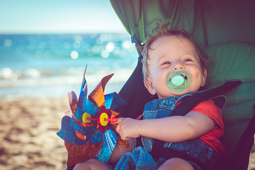 Cute baby sitting in stroller on the beach in summer